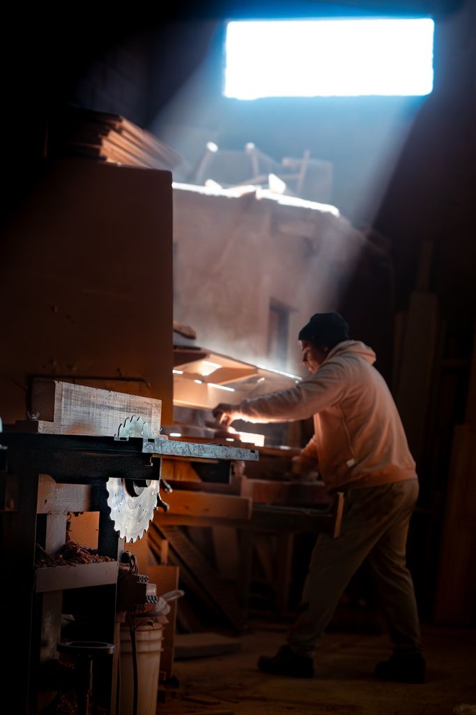 A dedicated craftsman working with wood in a dimly lit workshop, highlighted by a beam of light.
